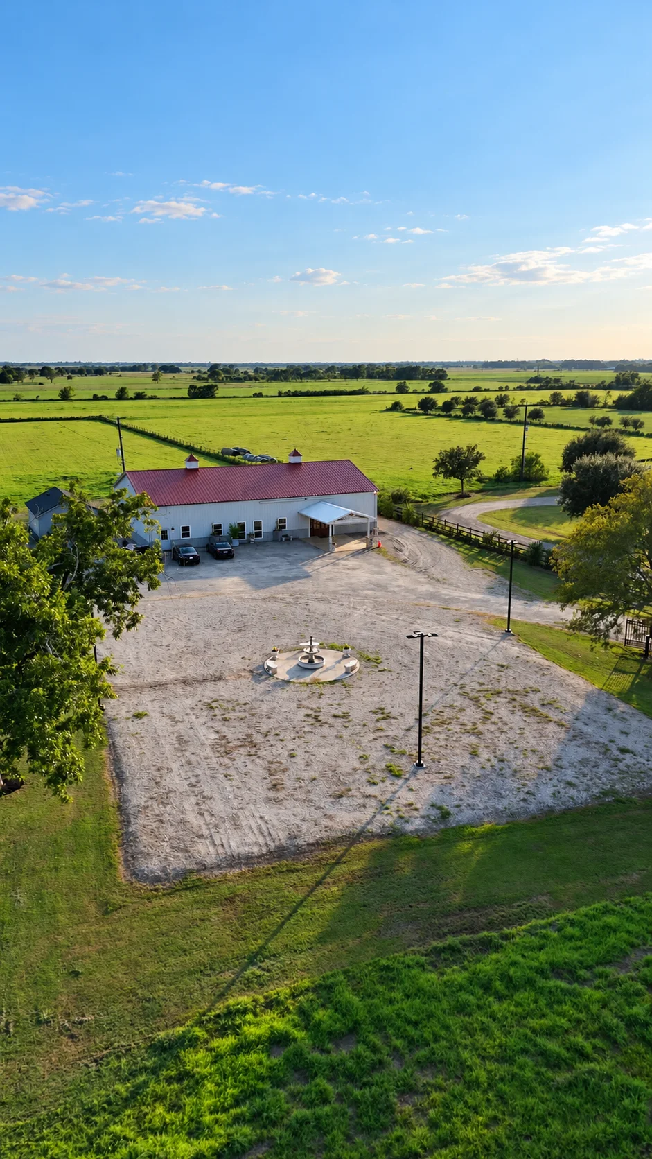 Full aerial view of the ranch hall, fountain in the gravel forecourt, and green fields