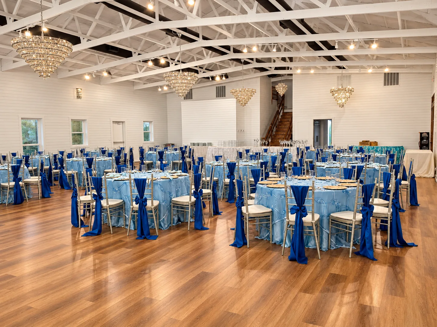 Wide view of the Texas AZ Paradise Ranch ballroom with white trusses, crystal chandeliers, wood floor, and blue banquet tables