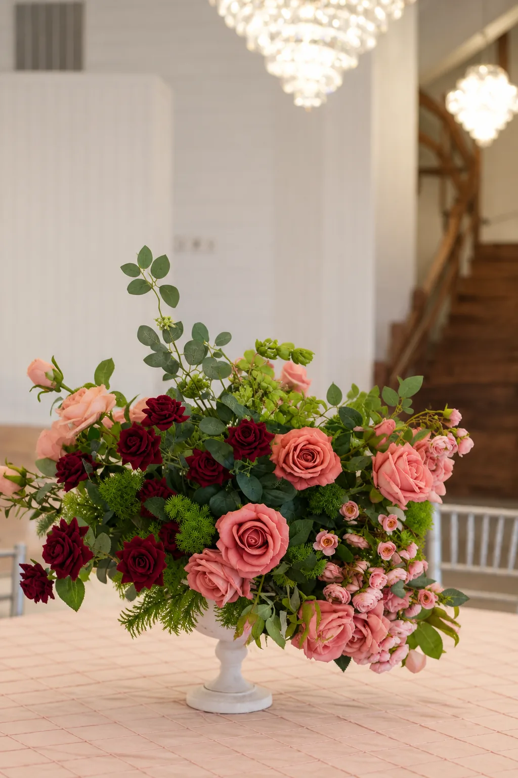 Pink and burgundy rose arrangement beneath a crystal chandelier inside the ballroom