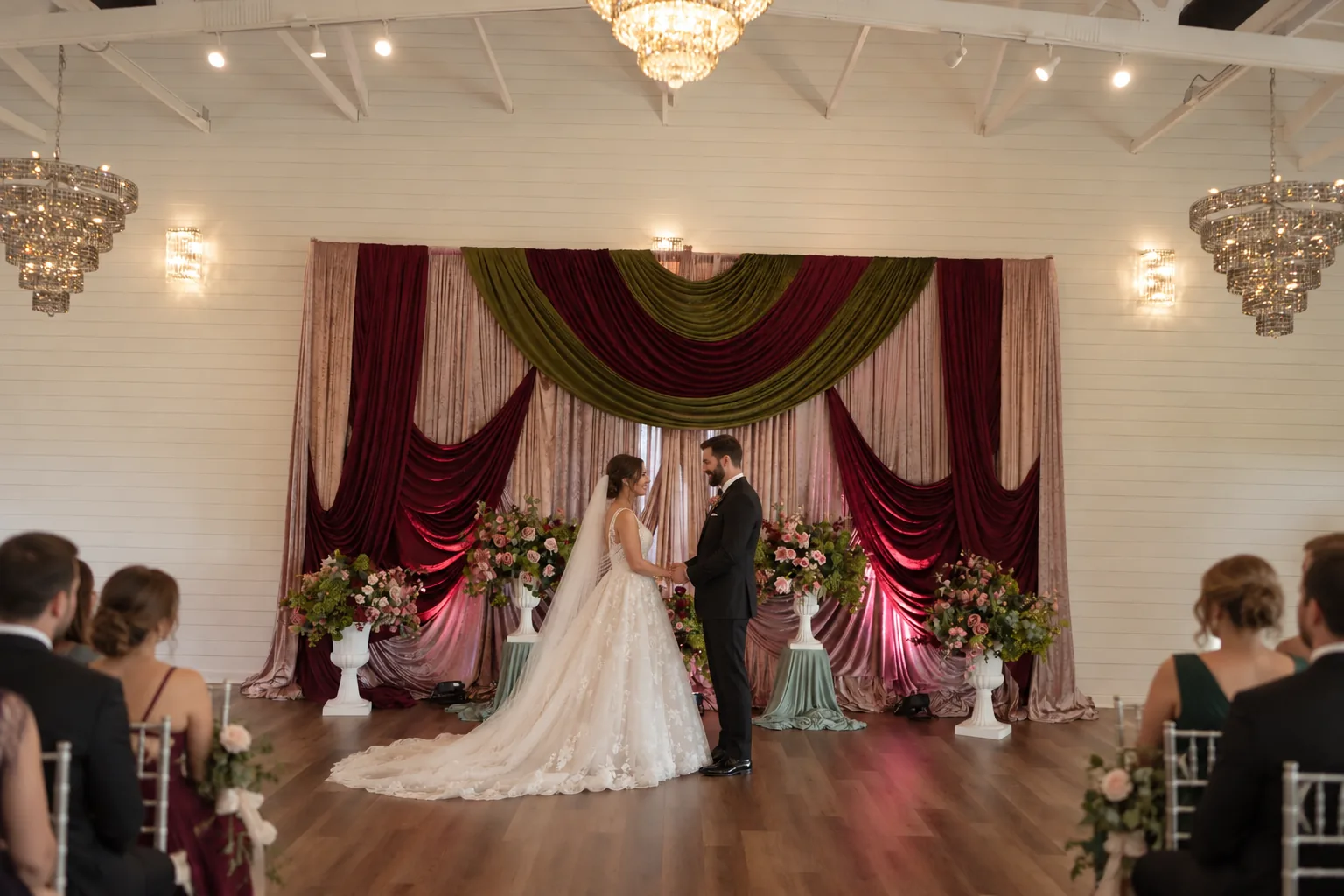 Wedding couple in front of the burgundy ceremony backdrop in the Richmond ranch hall.